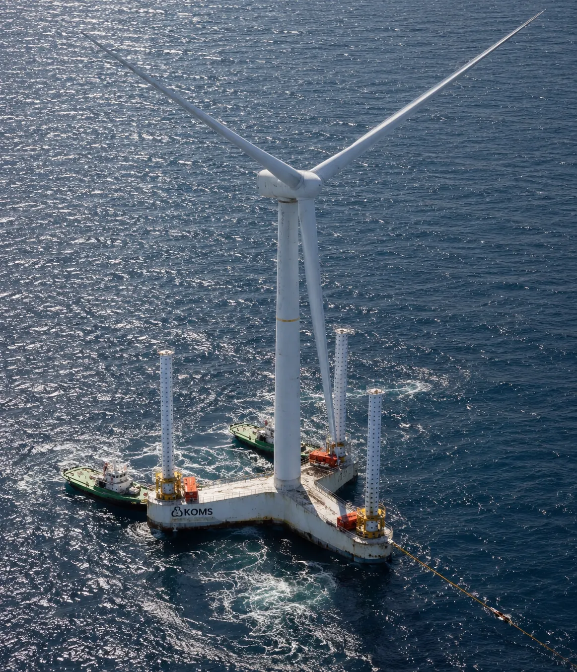 A semi-submersible floating wind platform at sea, its three buoyancy columns supporting a wind turbine, with two support vessels alongside and a mooring line running off from one corner