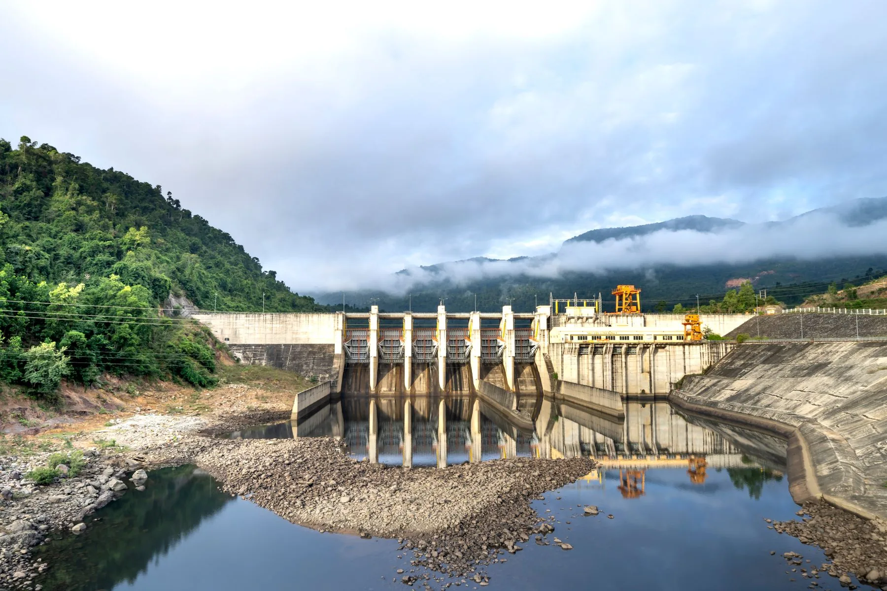 A hydroelectric dam on a river framed by green tropical mountains