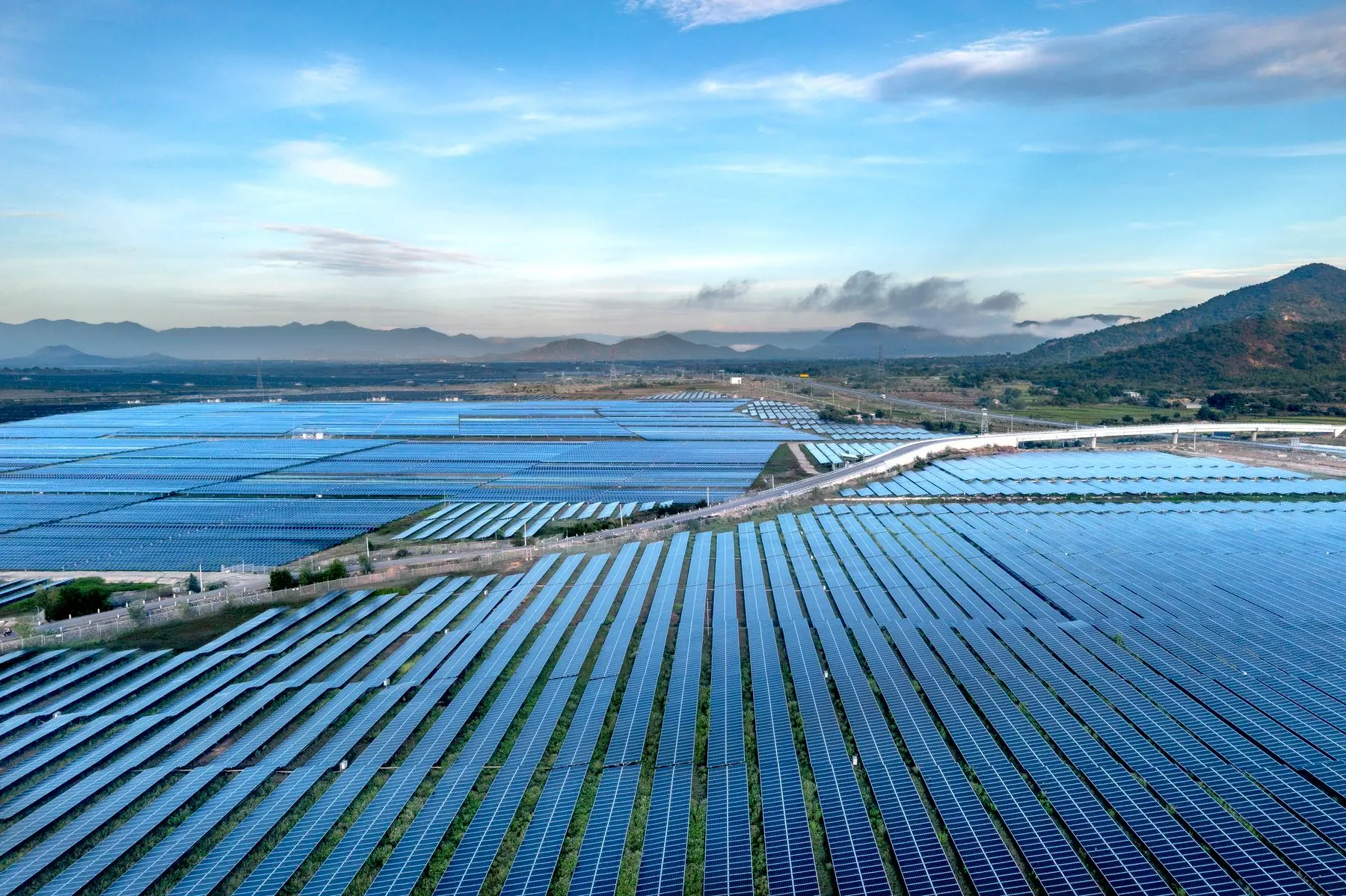 Aerial view of a vast solar panel farm stretching toward coastal mountains